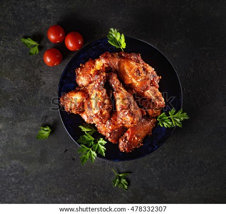 Fried chicken wings on rustic serving board, spicy tomato sauce, herbs and mug of light beer over black wooden backdrop, top view