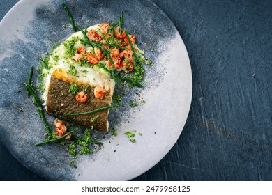 Fried cod fillet with mashed potatoes, fresh prawns and marsh samphire served as top view on a Nordic design plate with text space right