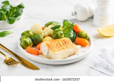 Fried cod fillet with steamed vegetables: baby carrots, Brussels sprouts, broccoli, cauliflower and corn salad on a white plate. Healthy food. Selective focus. - Shutterstock ID 1633072537