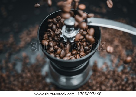 Fried coffee beans are falling to the manual grinder. Cinematic dark  colors. Preparation of fresh beverage morning coffee for breakfast. Mill for grinding. Isolated on black background.
