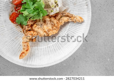 Fried crab presented with cherry tomatoes and cilantro on a textured white plate, set against a gray background for a modern culinary display