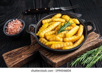 Fried Crinkle French fries potatoes in a pan. Black Wooden background. Top view