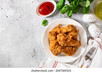 Fried crispy chicken legs in breadcrumbs in a white plate on a light culinary background. Fast food from the drumstick top view