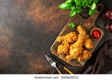 Fried crispy chicken legs in breadcrumbs on a wooden serving board on a dark background. Fast food from the drumstick top view	