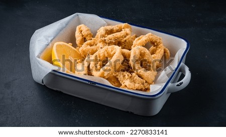 Fried crispy squid rings breaded ( caramari ) with lemon. Snack breaded squid rings with lemon on a dark background.