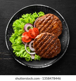 Fried Cutlet For Burger With Vegetables. In A Black Plate On A Wooden Background Top View. Free Space For Your Text. Flat Lay