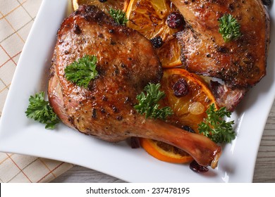 fried duck leg with oranges on a white plate, horizontal top view close-up 