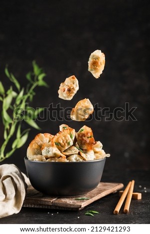 Fried dumplings with pork and herbs in a black round bowl and flying in the air on a dark background with chopsticks. Korean food. Side view with copy-paste for text. Vertical orientation.