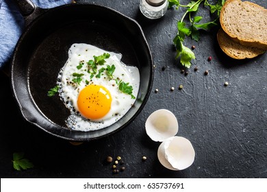 Fried egg. Close up view of the fried egg on a frying pan. Salted and spiced fried egg with parsley on cast iron pan and black background.