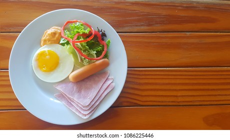 Fried egg, ham, sausage and salad in white plate on the wooden table. - Shutterstock ID 1086225446