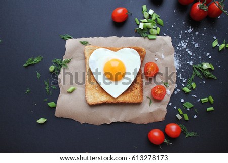 Fried egg on heart-shaped slice of toast on vintage black slate background. Cooking or healthy concept, with copy space for text, top view.