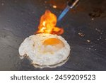 Fried egg on a hotplate to which the flame of a blowtorch is applied