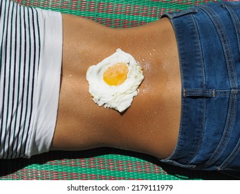 Fried Egg On Woman Sweaty Back With Jeans And Crop Top Laying On A Picnic Mat    