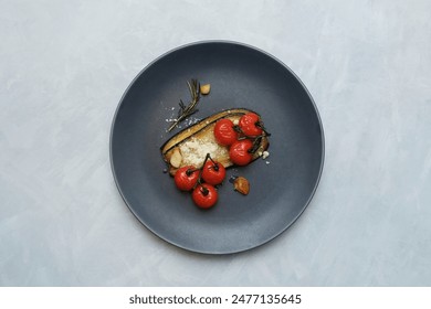Fried eggplant slices with parmesan cheese, cherry tomatoes, rosemary and garlic on dark plate, top view. - Powered by Shutterstock