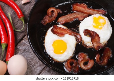 fried eggs with bacon in a frying pan and chili pepper, garlic on the table. top view 