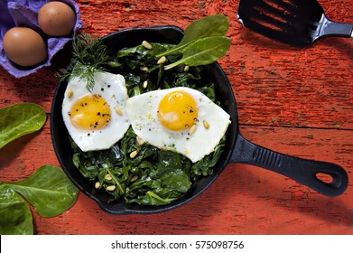 Fried eggs on spinach with pine nuts on iron skillet 