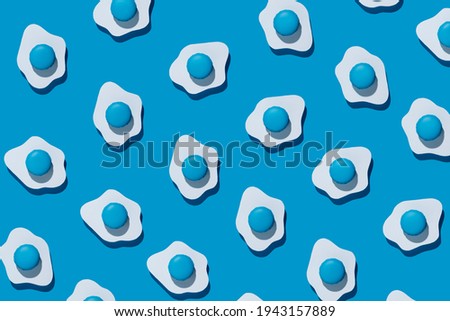 Fried eggs pattern made of paper on a vibrant blue background. Minimalistic food fashion concept. Flat lay, top view.