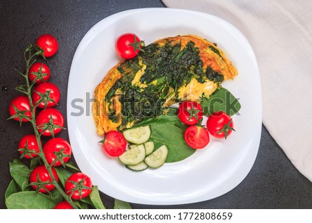 fried eggs with spinach and tomatoes, cucumbers on a white large plate on a black embossed table. top view, copy space