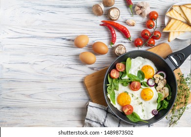 Fried Eggs With Tomatoes, Mushrooms And Spinach Leaves In Frying Pan On Table With Ingredients. Overhead Flat Lay