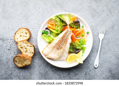 Fried Fillet Of Sea White Cod Fish With Juicy Lettuce, Capsicum, Lemon, Green Peas On A Large White Dish On A Gray Background. Healthy Balanced Food. Top View