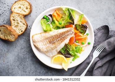 Fried Fillet Of Sea White Cod Fish With Juicy Lettuce, Capsicum, Lemon, Green Peas On A Large White Dish On A Gray Background. Healthy Balanced Food. Top View