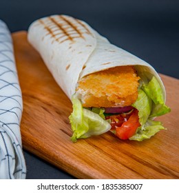 Fried Fish Fillet And Vegetables In Wheat Tortilla Wrap On The Wooden Deck