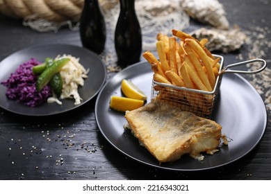 Fried Fish Fillets Served With Potato Fries In A Metal Serving Basket And Salad Mix, On Black Plates, Selective Focus.