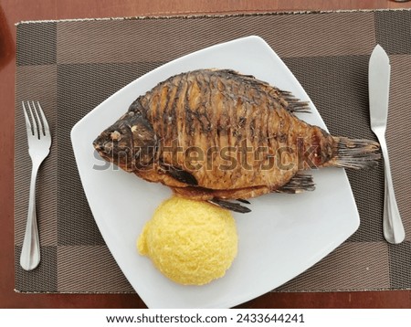 Fried fish on a square plate, together with polenta, waiting to be served, with fork and knife