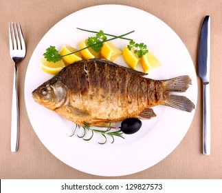 Fried fish on white plate with fork and knife, closeup
