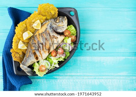 Fried fish with salad and patacones on a blue background. Copy space.