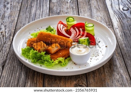 Fried fish sticks with fresh vegetables on wooden table 