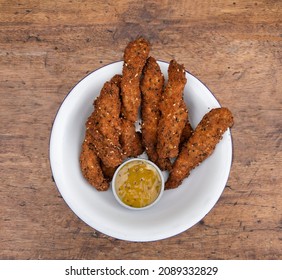 Fried Gourmet Food. Overhead View Of Deep Fried Chicken Sticks Breaded With Seeds And A Dip Made Of Mustard And Honey, In A White Bowl On The Table. 