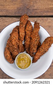 Fried Gourmet Food. Overhead View Of Deep Fried Chicken Sticks Breaded With Seeds And A Dip Made Of Mustard And Honey, In A White Bowl On The Table.