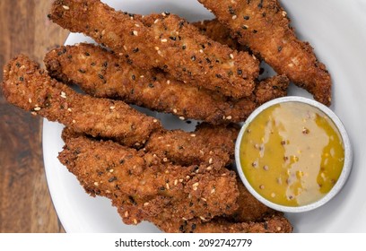 Fried Gourmet Food. Overhead View Of Deep Fried Chicken Sticks Breaded With Seeds And A Dip Made Of Mustard And Honey, In A White Bowl On The Table. 