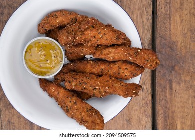 Fried Gourmet Food. Overhead View Of Deep Fried Chicken Sticks Breaded With Seeds And A Dip Made Of Mustard And Honey, In A White Bowl On The Table.