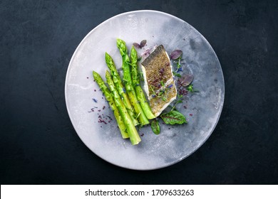 Fried gourmet skrei cod fish filet with green asparagus and lettuce offered as top view on a modern design plate with copy space  - Powered by Shutterstock