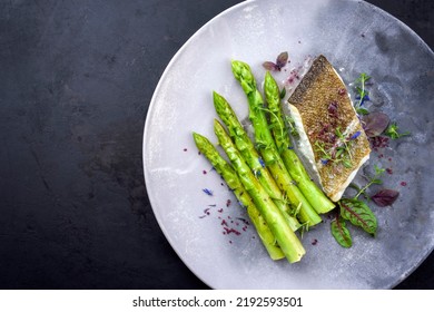 Fried gourmet skrei cod fish filet with green asparagus and lettuce offered as top view on a modern design plate with copy space left - Powered by Shutterstock