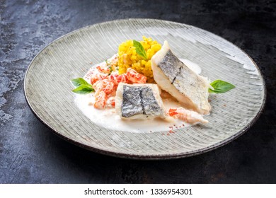 Fried Haddock Filet With Saffron Rice And Shell Prawns In Crab Sauce As Closeup On A Modern Design Plate