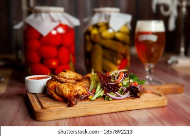Fried juicy chicken with vegetables and herbs and a glass of light beer on the table in the bar in dark colors