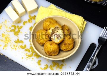 Fried macaroni cheese balls, served on a ceramic plate with raw macaroni and cheese around