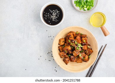 Fried marinated tofu cubes in bamboo bowl served with chopped scallions, sesame seed oil and soy sauce. Top view copy space. Asian cuisine