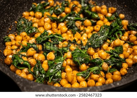 fried Mediterranean middle eastern chickpeas with spinach in frying pan skillet on home kitchen stove. delicious tasty vegan health food pulses and leafy green vegetable