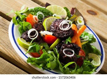 Fried morcilla (blood sausage with rice) served with vegetable salad from tomatoes, carrots and assorted greens