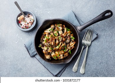 Fried mushrooms with fresh herbs in black cast iron pan. Top view.