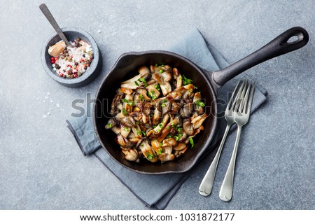 Fried mushrooms with fresh herbs in black cast iron pan. Top view.