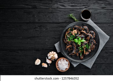 Fried mushrooms with parsley on the plate. On a black background. Top view. Free space for your text.