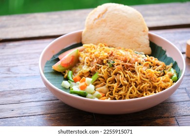 Fried noodles with cucumber and carrot pickles and sliced tomatoes in bowl. The bowl on wooden table. Mie goreng - Shutterstock ID 2255915071