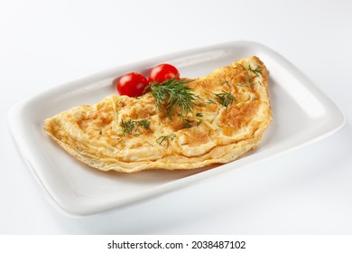 Fried omelet, folded in half, sprinkled with fresh dill and served with fresh cherry tomatoes on a white flat rectangular ceramic plate on a white background