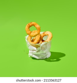 Fried onion rings in paper bag on green background. Flying onion rings in minimal style. Fast food appetizer in contemporary concept. Junk food on color background. Fast food menu