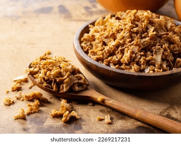 Fried onions in bowl on wooden background with wooden spoon. Crispy fried onions.